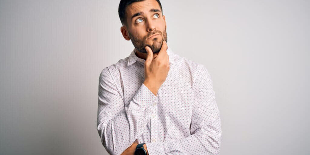 Young handsome man wearing elegant shirt standing over isolated white background with hand on chin thinking about question, pensive expression. Smiling with thoughtful face. Doubt concept.