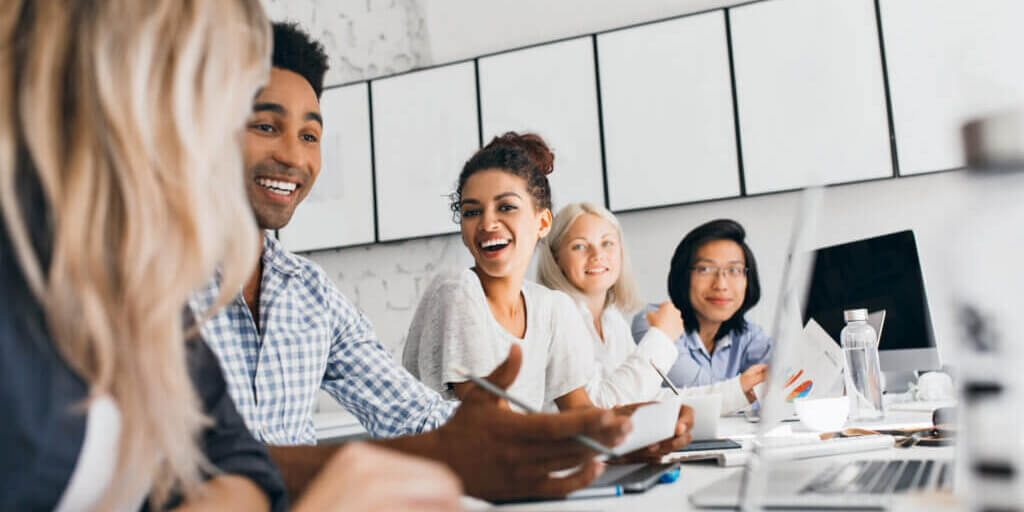 Young entrepreneurs discussing something with smile during conference. Indoor portrait of international employees sitting in office with laptops and talking about work.
