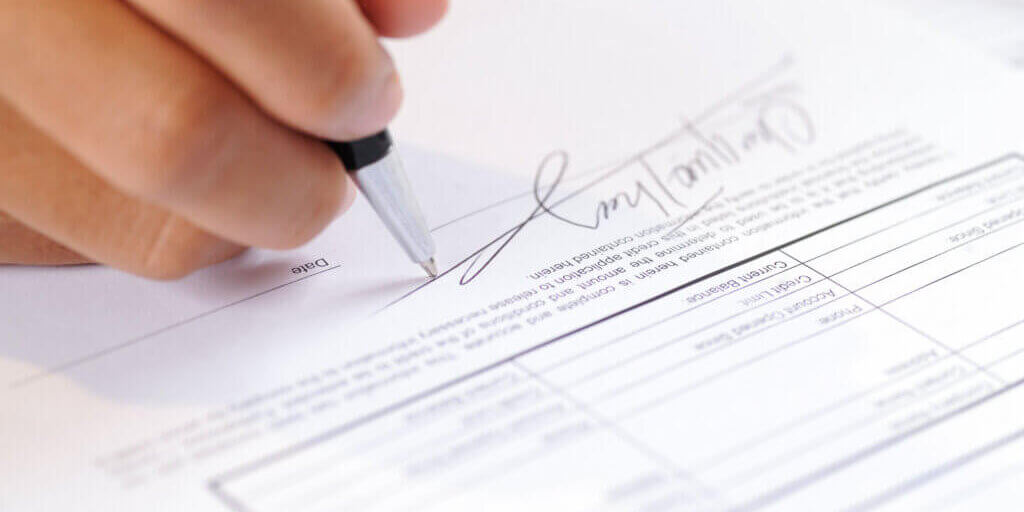 Closeup of person signing document with ball pen. Contract lying on table. Agreement concept. Cropped view.