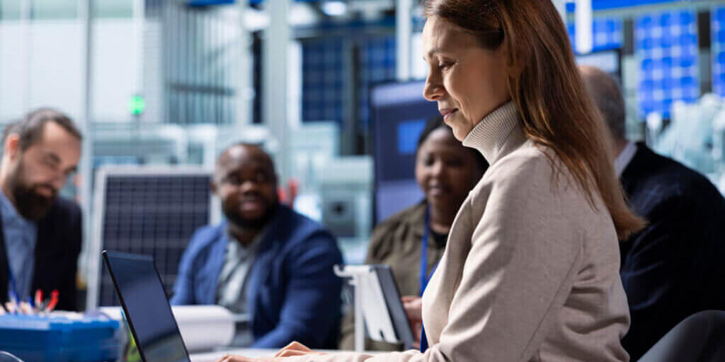 Photovoltaics factory management team analyzing data using laptop, reviewing system health metrics. Solar panels manufacturing plant executives troubleshooting technical issues using notebook