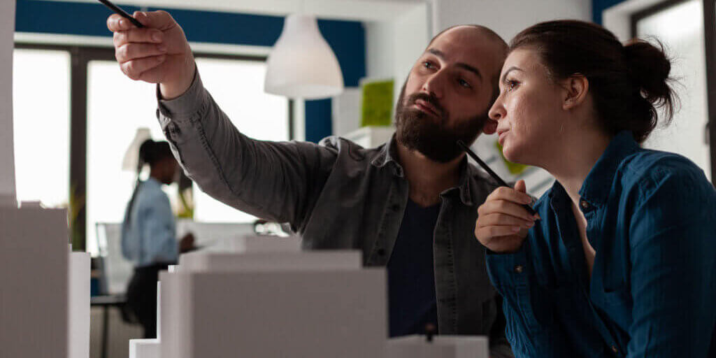 Architectural designers team pointing pen at skyscraper discussing architecture design in modern office. Architects colleagues brainstorming ideeas collaborating on white foam model.