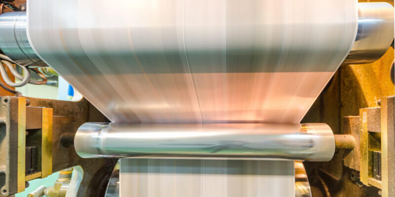 A large webset offset printing press running a long roll off paper over its rollers at high speed.