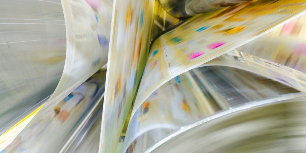 A large webset offset printing press running a long roll off paper over its rollers at high speed.