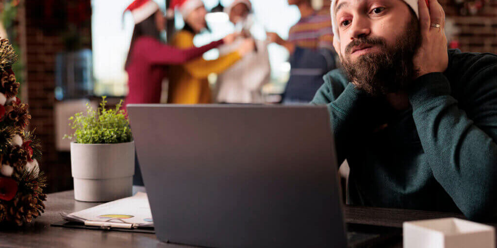 Stressed tired company worker having burnout while managing workload on laptop in xmas decorated office. Exhausted caucasian man in santa hat sitting at workplace during new year holiday
